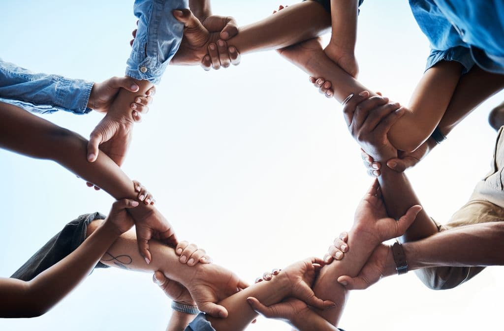 Hands of diverse skin tones holding each other by the wrists to form a connected circle.